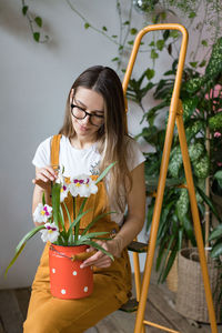 Woman with potted plant sitting on ladder in workshop