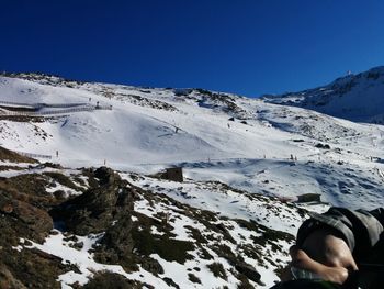 Low section of man on snowcapped mountain against clear blue sky