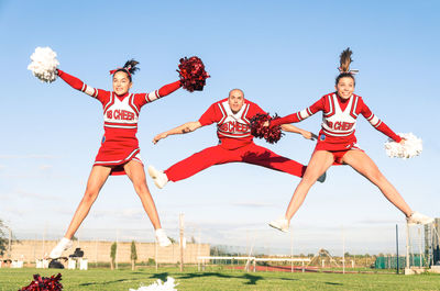 Cheerleaders performing with sportsman on field against blue sky