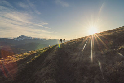 People walking on road against sky during sunset