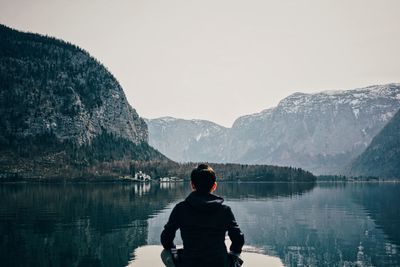 Rear view of man looking at lake against mountain range