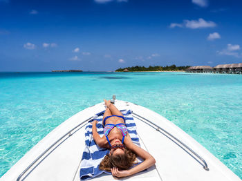 Young woman wearing bikini relaxing on boat in sea against sky during sunny day