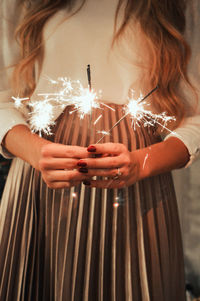 Midsection of woman holding sparkler at night