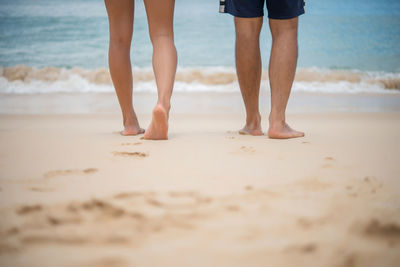 Low section of couple walking at beach