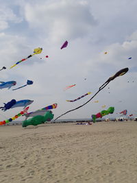 Kites flying over beach against cloudy sky