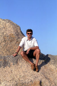 Young man wearing sunglasses on rock against clear sky