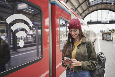 Smiling woman using mobile phone by train at railroad station