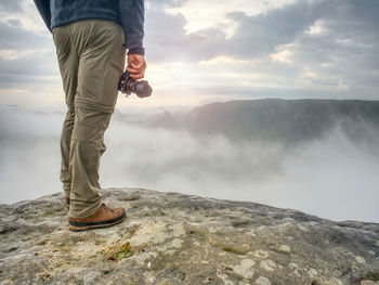 Landscape photograper with camera ready in hand. man climbed up on exposed rock for fall photos