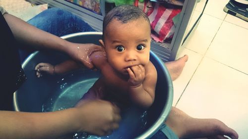 Low section of mother bathing baby boy in tub at home