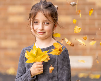 Portrait of smiling girl holding leaves while standing outdoors