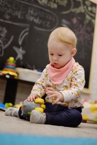 Cute baby girl playing with toys while sitting on rug at home