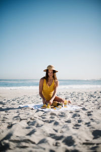 Young woman sitting on beach against clear sky