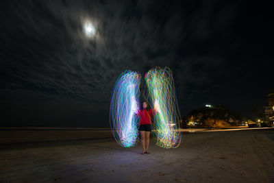 Illuminated light trails on beach against sky at night