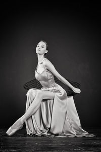 Portrait of a ballerina in a pink dress is sitting on a chair with her leg in the slit of the dress