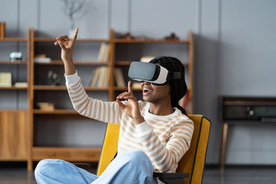 Excited african woman leaning on chair wearing vr headset playing in virtual games during work break