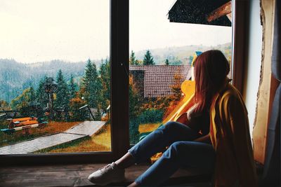 Woman looking through window while sitting at home during rainy season