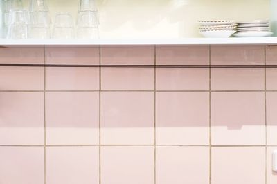 Glasses and plates on shelf over tiled wall in kitchen