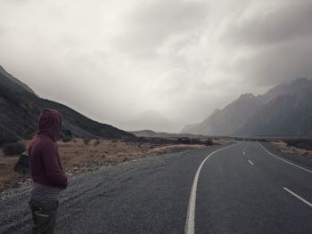 Person waiting on mountain road against sky