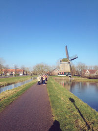 People on footpath by canal against clear sky
