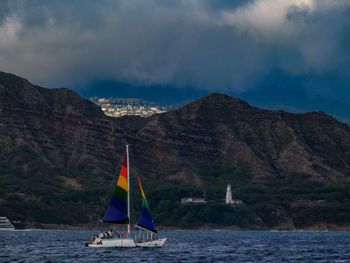 Sailboat sailing on sea by mountains against sky