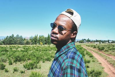 Portrait of young man standing on field against clear sky