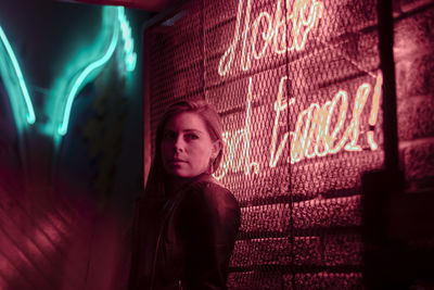 Young woman looking away by illuminated wall