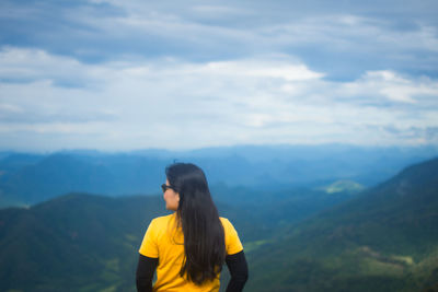 Rear view of woman standing on mountain against sky