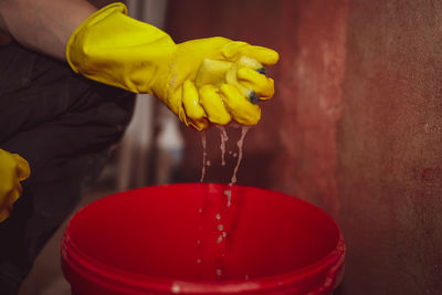 Caucasian male builder in yellow gloves squeezes a sponge.