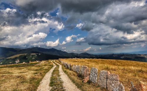 Empty road amidst field against sky