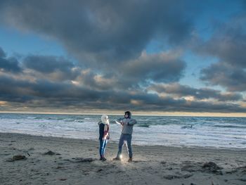 People on beach against cloudy sky