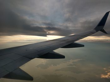Airplane wing flying over clouds during sunset