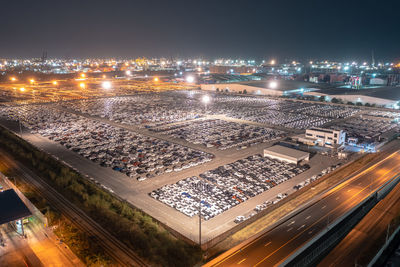 New cars parked at distribution center automobile factory at night with lights and commercial dock 