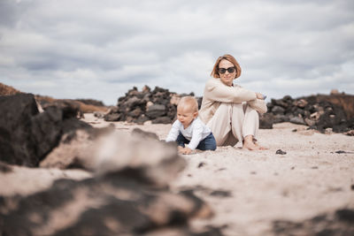 Mother enjoying winter beach vacations playing with his infant baby boy son on wild volcanic sandy