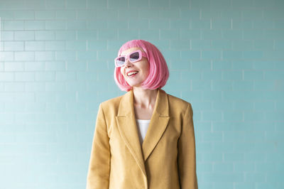 Smiling woman with sunglasses standing near turquoise wall