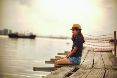 Woman sitting on pier over lake during sunset