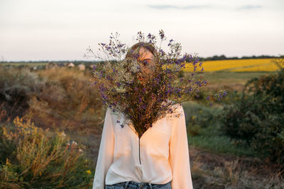 Midsection of woman standing by flowering plant on field against sky