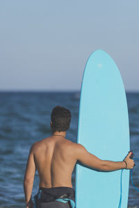 Rear view of shirtless boy in sea against clear sky