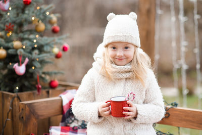Cute smiling kid girl 4-5 year old drink hot chocolate with red candy stick in mug