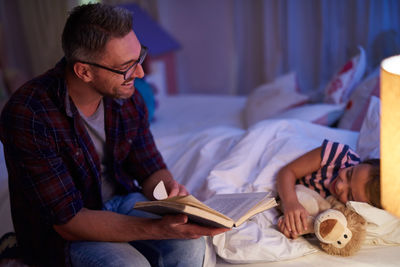 Smiling father reading a bedtime story for daughter at home