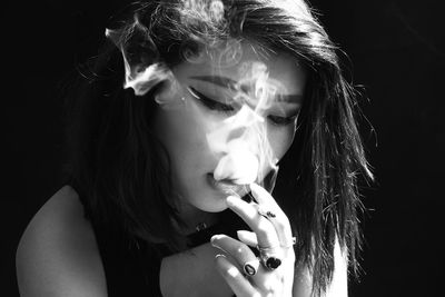 Close-up of young woman smoking over black background