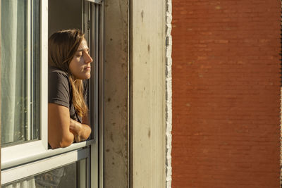 Side view of woman with eyes closed standing at window