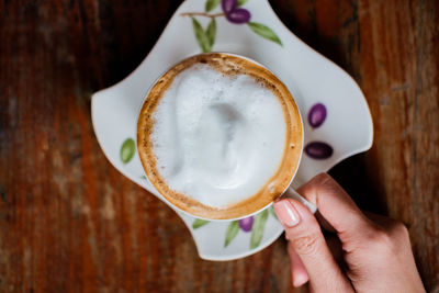 Close-up of woman holding coffee cup on table