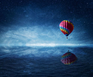 Hot air balloon flying over sea against blue startul night sky