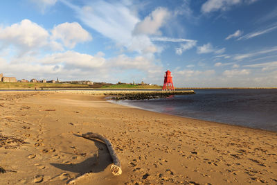 Driftwood on sand with lighthouse at beach against sky