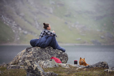 Man sitting on rock at shore against mountains