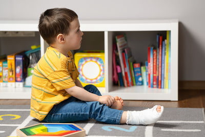 A little toddler boy 3 years sitting with a cast in a leg in a children room. fracture of a foot 