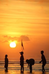 Silhouette people on beach against orange sky