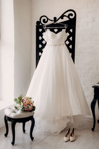 Wedding dress hanging on coat hanger against white wall