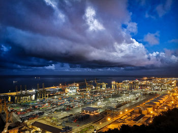 High angle view of illuminated city by sea against sky