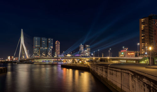 Bridge over river by illuminated buildings in city at night